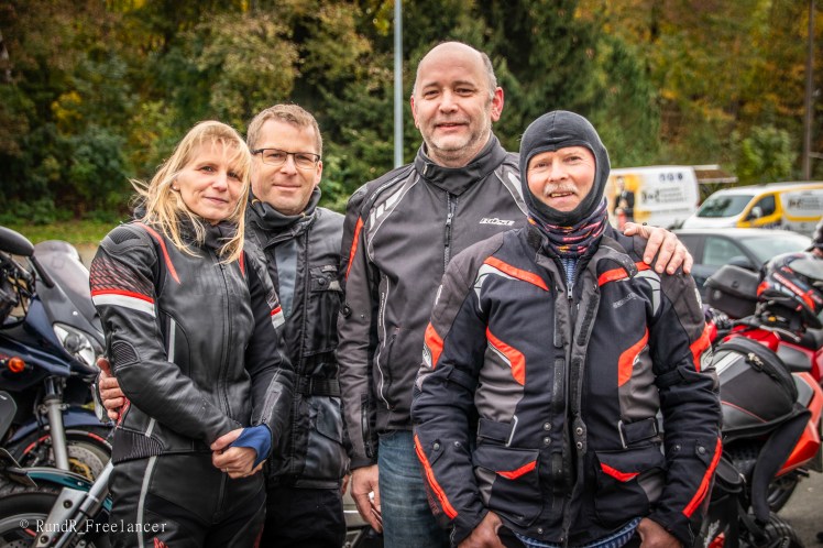Vier Motorradfahrer in Schutzkleidung posieren gemeinsam vor ihren Motorrädern bei herbstlicher Umgebung.
